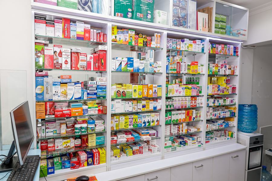 Floor-to-ceiling white pharmacy shelving with glass shelves and upper display cabinets, Ngong