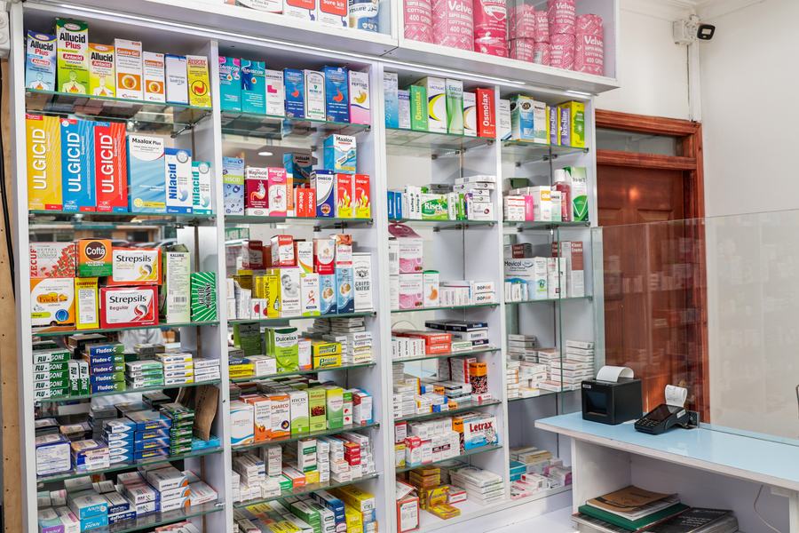 Pharmacy shelving beside the payment counter with glass sneeze guard, Kenri Pharmacy Ngong