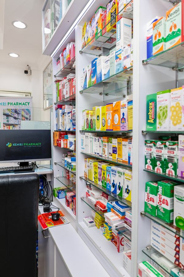 Pharmacy aisle with lit display shelving, Kenri Pharmacy Ngong — portrait view